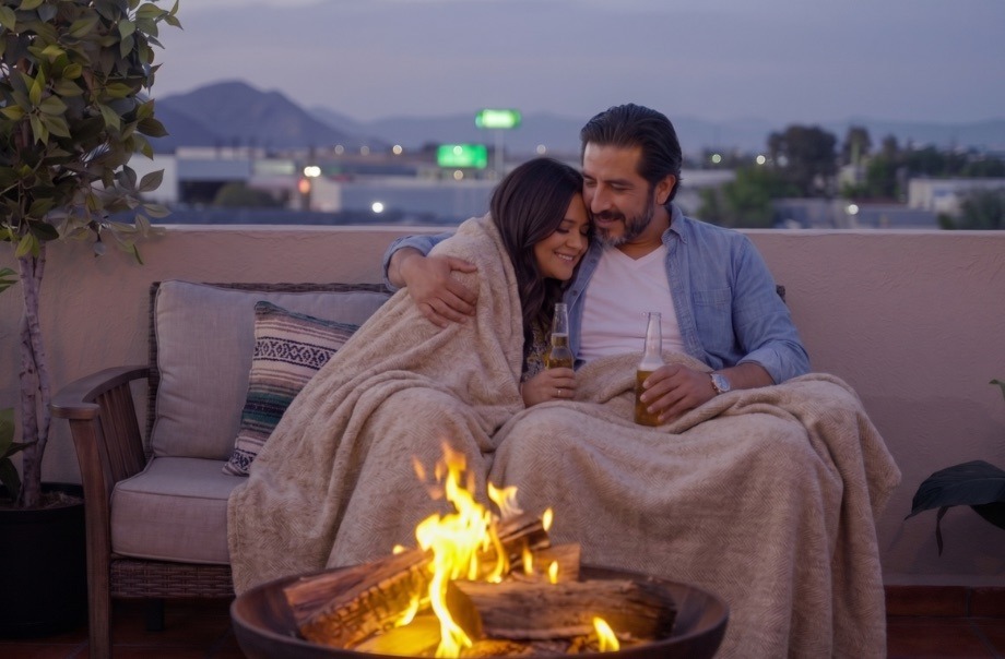Pareja con cobija junto a una fogata en la terraza al anochecer