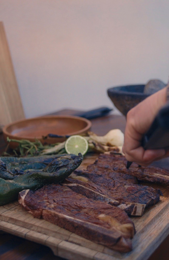 Cortes asados sobre tabla de madera con chiles toreados y limón