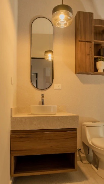 Baño con lavabo sobre mueble de madera y espejo ovalado